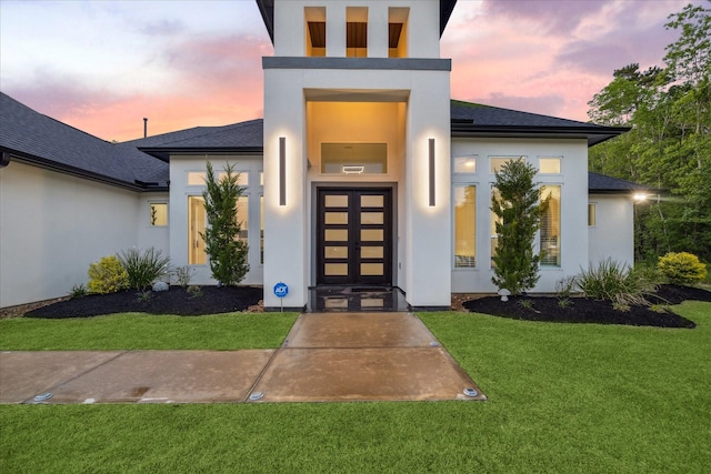 doorway to property featuring a shingled roof, stucco siding, and a yard