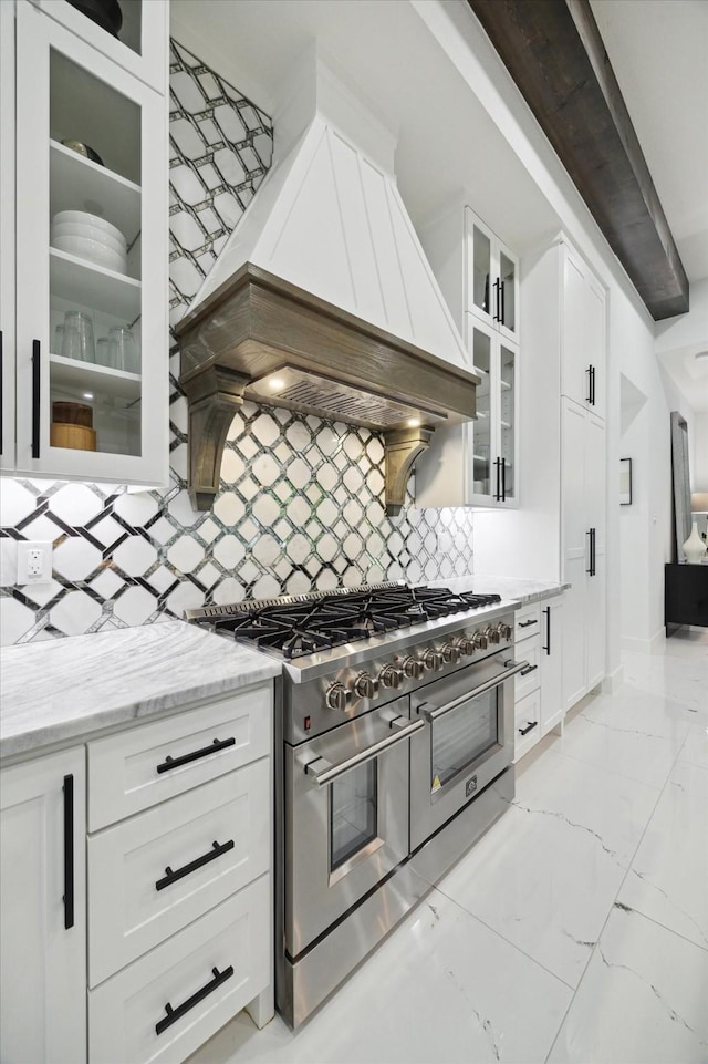 kitchen with decorative backsplash, marble finish floor, light stone countertops, premium range hood, and double oven range
