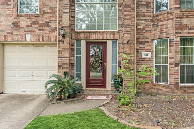 view of exterior entry with brick siding, driveway, and a garage