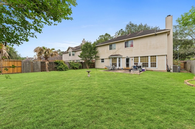 rear view of property featuring a chimney, cooling unit, a fenced backyard, a yard, and a patio