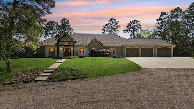view of front of property featuring a lawn, driveway, stone siding, a tiled roof, and a garage