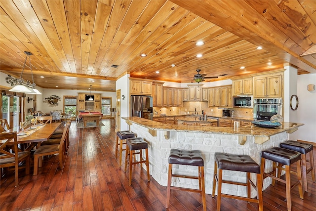 kitchen featuring light stone counters, wood ceiling, a kitchen bar, appliances with stainless steel finishes, and dark wood-style floors