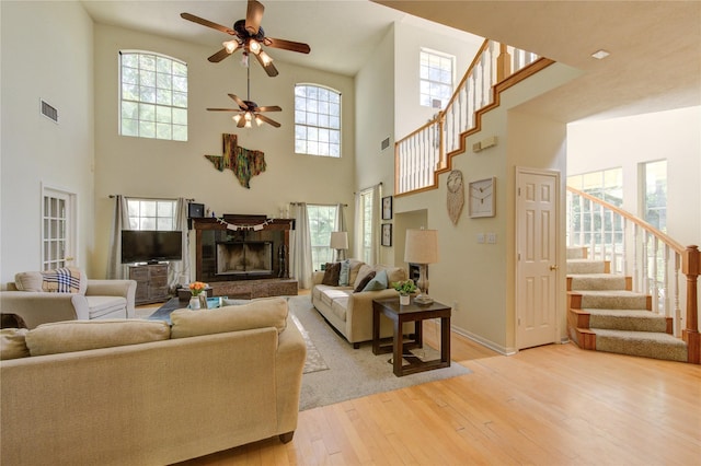 living area featuring stairway, a high ceiling, a ceiling fan, light wood-type flooring, and a wealth of natural light