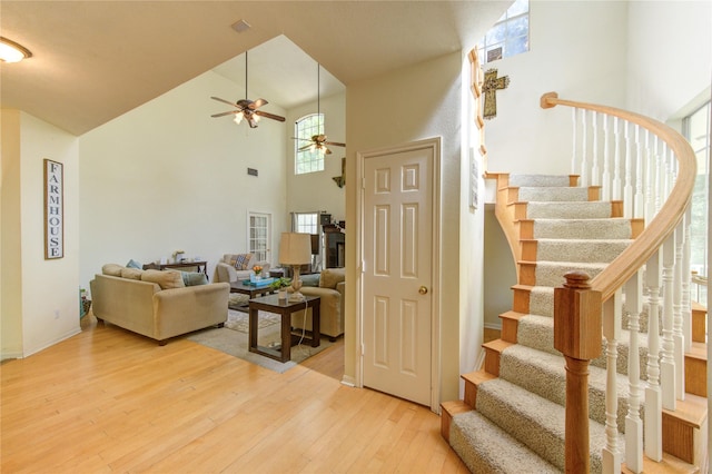 staircase featuring hardwood / wood-style floors, a ceiling fan, baseboards, and high vaulted ceiling