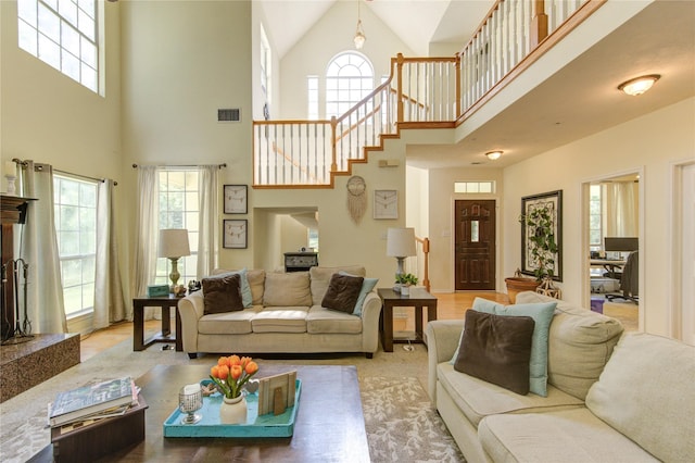living room featuring stairway, visible vents, a healthy amount of sunlight, and a high ceiling