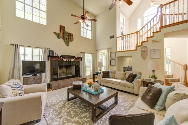 living area featuring high vaulted ceiling, stairway, a ceiling fan, a fireplace, and visible vents