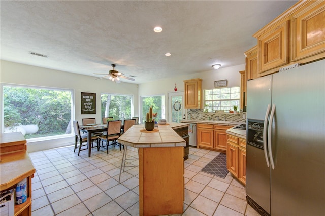 kitchen with tile counters, stainless steel appliances, visible vents, a center island, and decorative backsplash