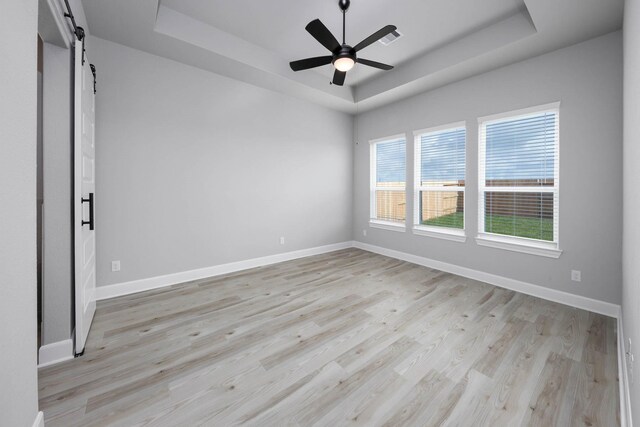 empty room with baseboards, light wood-type flooring, and a raised ceiling