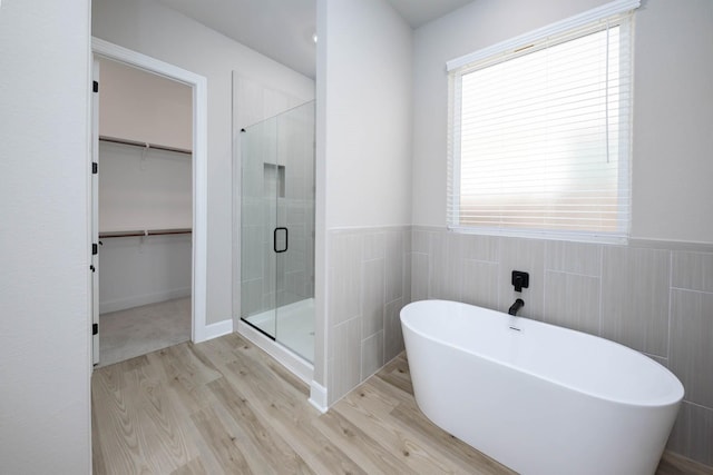 bathroom featuring a freestanding bath, wood finished floors, a spacious closet, and a stall shower