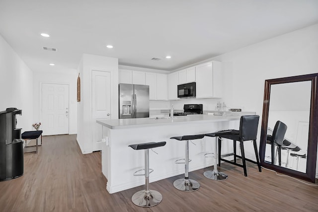 kitchen with a peninsula, light countertops, wood finished floors, and black appliances