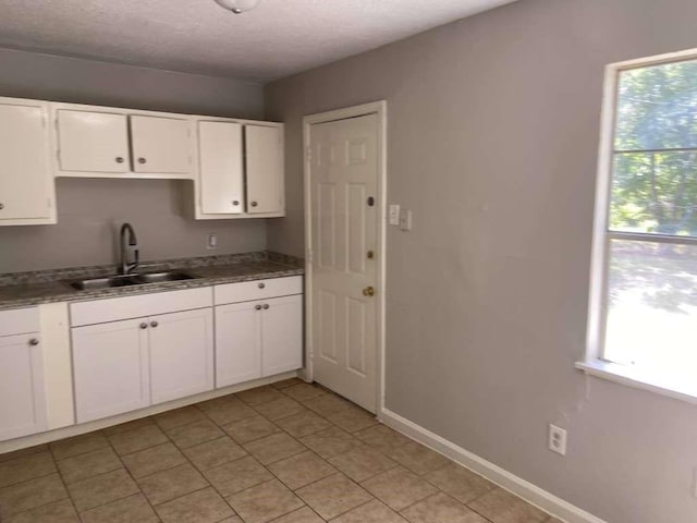 kitchen featuring white cabinets, a textured ceiling, baseboards, and a sink
