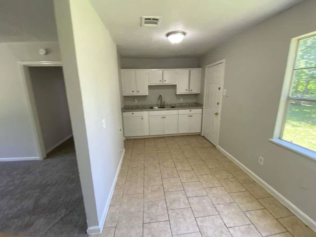 kitchen featuring white cabinets, baseboards, visible vents, and a sink