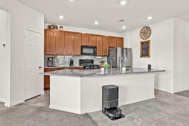 kitchen featuring recessed lighting, dark stone countertops, visible vents, a kitchen island with sink, and black appliances