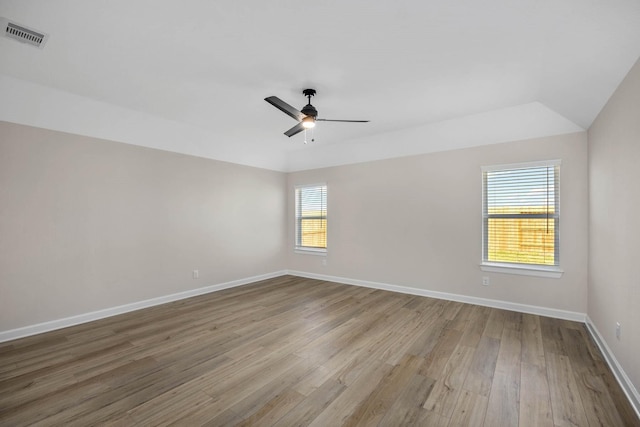 unfurnished room with a ceiling fan, visible vents, vaulted ceiling, wood finished floors, and baseboards