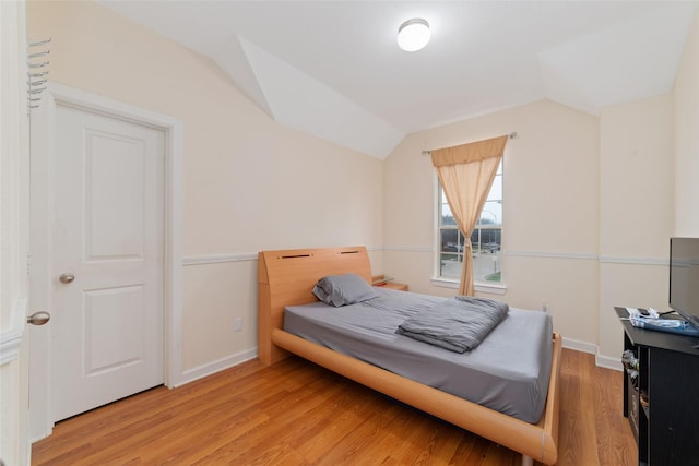bedroom with vaulted ceiling, baseboards, and light wood-style flooring