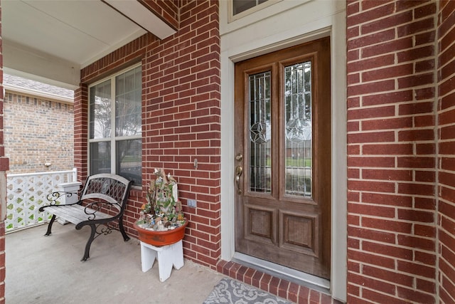 view of exterior entry featuring brick siding and a porch
