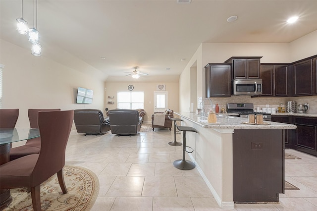 kitchen featuring stainless steel appliances, dark brown cabinets, a kitchen bar, decorative backsplash, and a ceiling fan