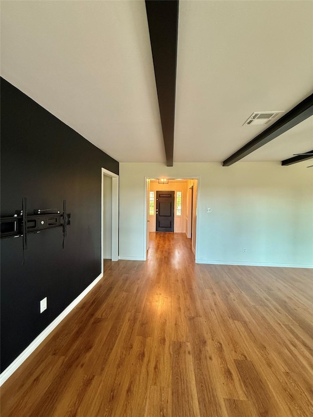 spare room with beamed ceiling, wood finished floors, visible vents, and baseboards