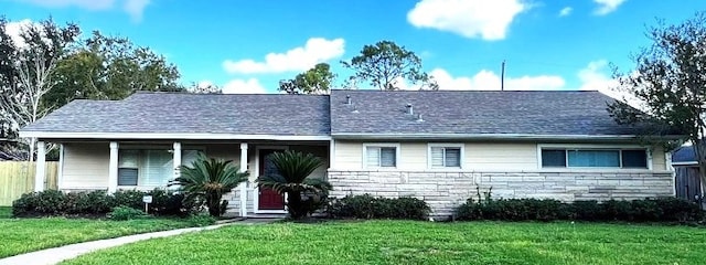 view of front facade featuring covered porch, fence, stone siding, and a front lawn