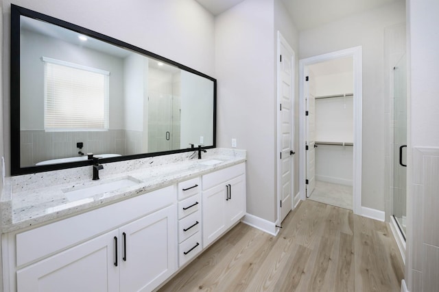 bathroom featuring a sink, double vanity, a stall shower, a spacious closet, and wood finished floors