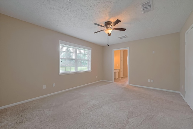 spare room with light carpet, a textured ceiling, visible vents, baseboards, and a ceiling fan