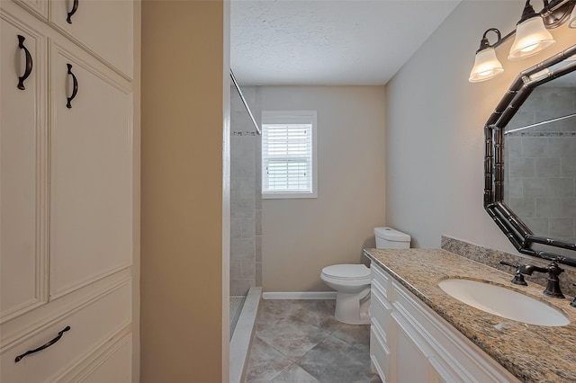 bathroom featuring a tile shower, toilet, vanity, baseboards, and a textured ceiling