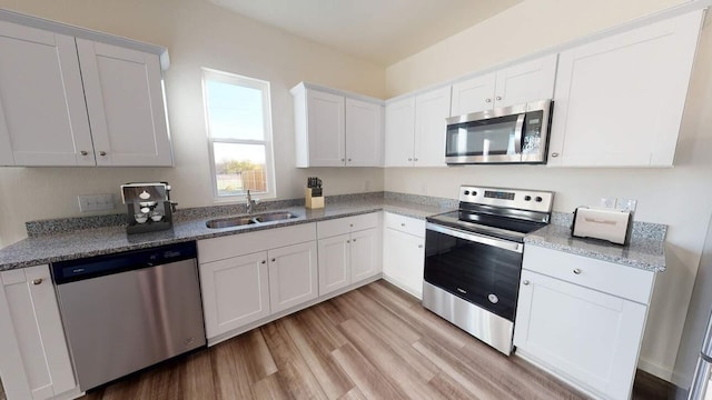 kitchen featuring light wood finished floors, a sink, white cabinetry, light stone counters, and appliances with stainless steel finishes