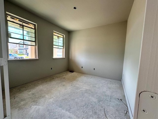 spare room featuring baseboards and unfinished concrete flooring