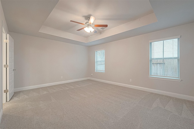 empty room featuring a raised ceiling, a ceiling fan, and baseboards