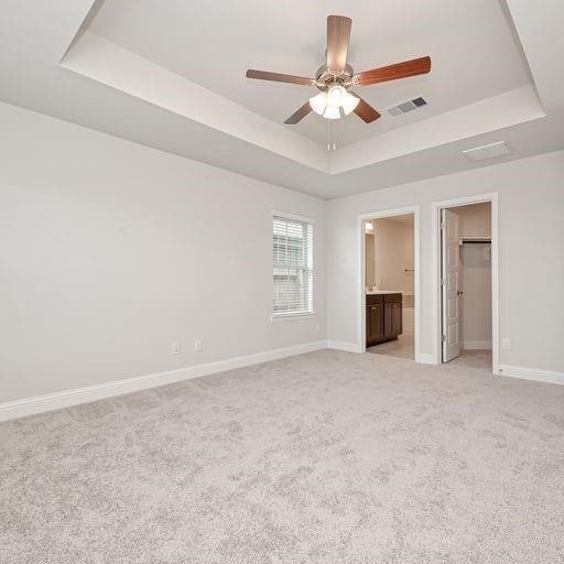 unfurnished bedroom featuring a walk in closet, light carpet, a raised ceiling, baseboards, and visible vents