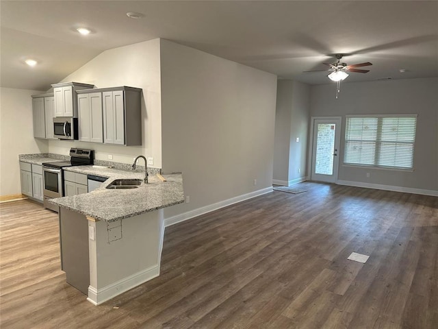 kitchen with a sink, open floor plan, ceiling fan, light stone countertops, and appliances with stainless steel finishes