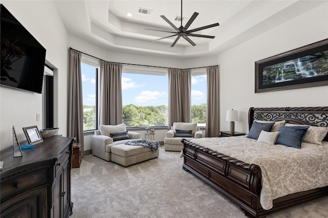 bedroom featuring a ceiling fan, light carpet, a tray ceiling, and visible vents