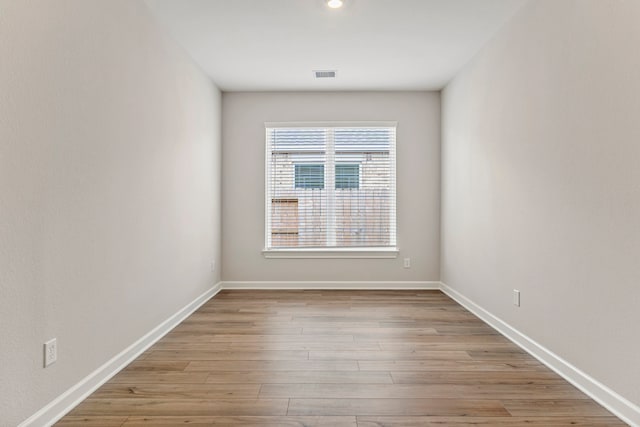 empty room with wood finished floors, visible vents, and baseboards