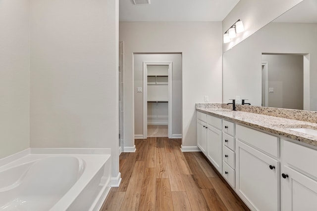full bathroom with a spacious closet, wood finished floors, double vanity, a sink, and a bath