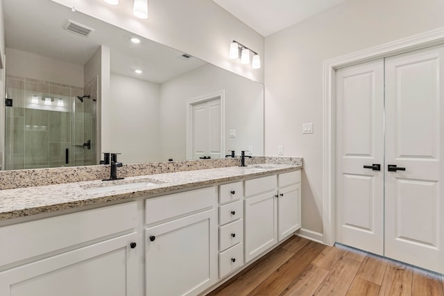 bathroom with wood finished floors, visible vents, a sink, and a shower stall