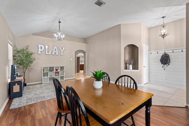 dining space featuring vaulted ceiling, wood finished floors, arched walkways, a notable chandelier, and visible vents