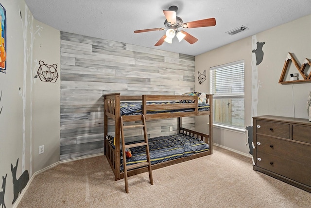 bedroom with carpet, visible vents, a ceiling fan, an accent wall, and baseboards