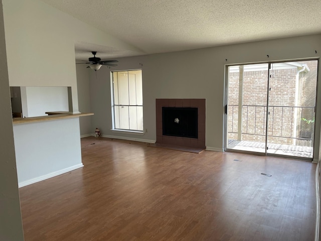 unfurnished living room with a tile fireplace, vaulted ceiling, wood finished floors, a ceiling fan, and a textured ceiling