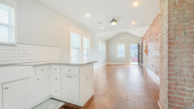 kitchen with light stone counters, a ceiling fan, hardwood / wood-style floors, a peninsula, and white cabinetry
