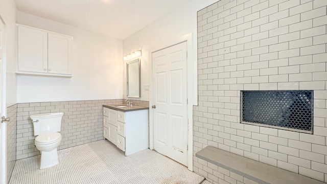 full bath featuring tile patterned floors, vanity, tile walls, a wainscoted wall, and toilet