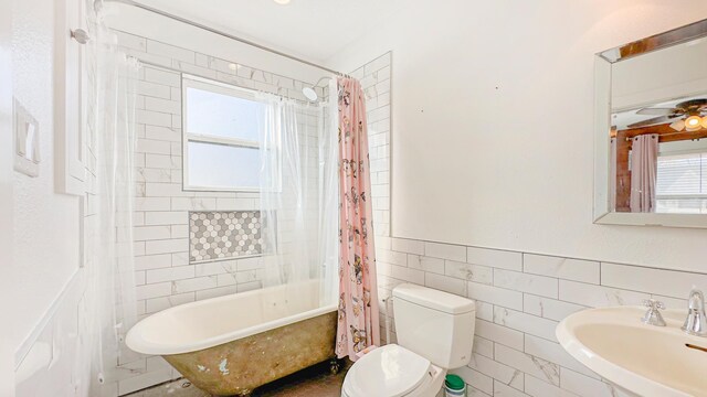 bathroom featuring a sink, shower / bathtub combination with curtain, tile walls, a wainscoted wall, and toilet