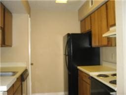 kitchen featuring white range with electric stovetop, brown cabinets, light countertops, under cabinet range hood, and freestanding refrigerator