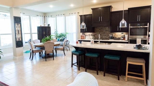 11903 Muir Groves Trl, Humble, TX 77346 - kitchen featuring stainless steel double oven, a kitchen bar, backsplash, light countertops, and hanging light fixtures