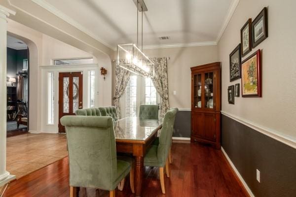 dining space with arched walkways, dark wood-style flooring, ornamental molding, and visible vents