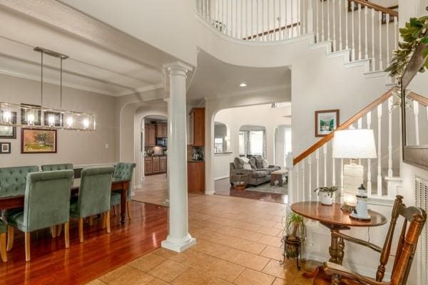 interior space featuring arched walkways, ornate columns, a high ceiling, stairs, and crown molding
