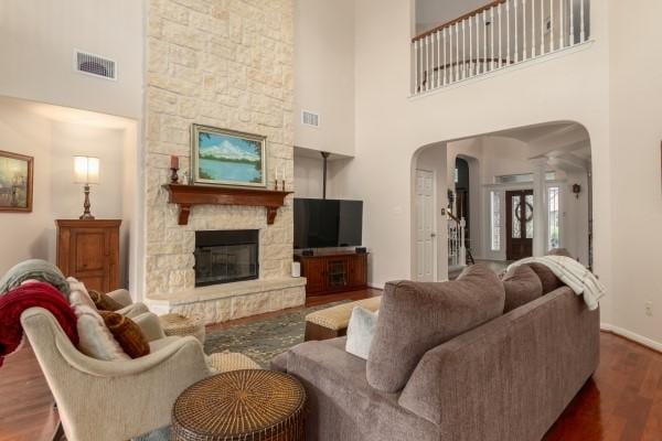 living room with wood finished floors, arched walkways, a fireplace, a high ceiling, and visible vents
