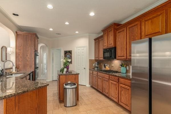 kitchen with a center island, a sink, black microwave, arched walkways, and freestanding refrigerator