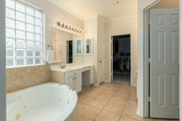 bathroom featuring a spacious closet, tile patterned floors, vanity, a tub with jets, and ornamental molding