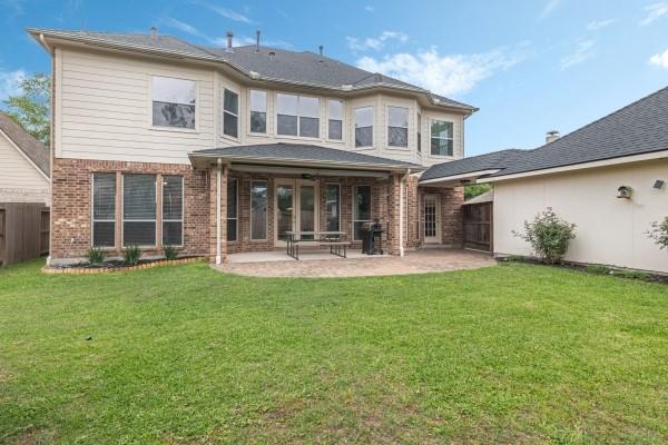 rear view of house with brick siding, a yard, a patio area, and fence