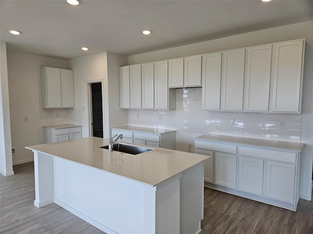 kitchen featuring wood finished floors, a sink, decorative backsplash, an island with sink, and white cabinetry